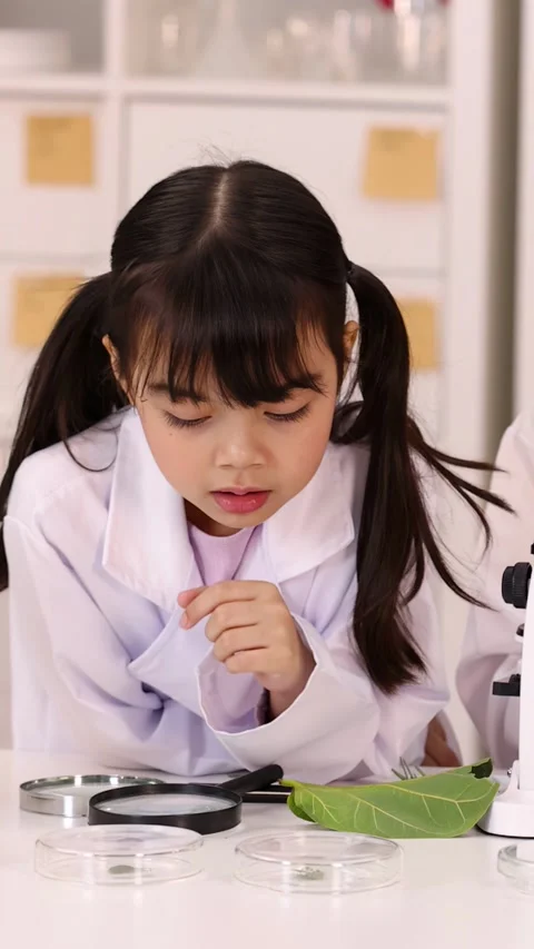 Young Girl in Lab Coat Studying Plant Leaf with Magnifying Glass Stock Footage 346124481