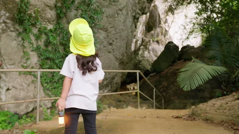 Young girl with a lantern prepares to explore the entrance of a dark cave Stock Footage 344139517
