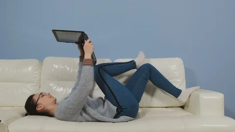 A young girl lies on a sofa with a computer in her hands Stock Footage 129506544