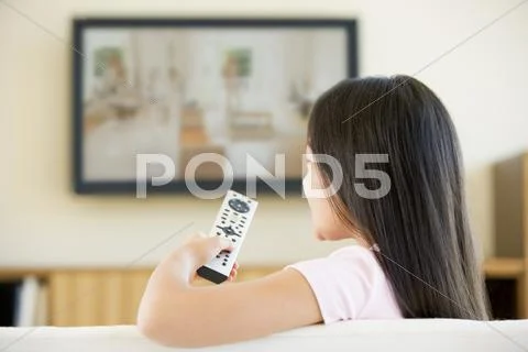 Young girl in living room with flat screen television and remote control Stock-Fotos