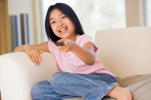 Young girl in living room with remote control smiling Stock Photos
