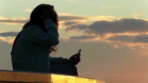 Young girl with long hair sit on the parapet and use video calling on smartphone Stock Footage