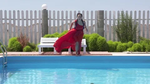 Young girl in long red dress jumping into outdoor swimming pool in slow motion Stock Footage