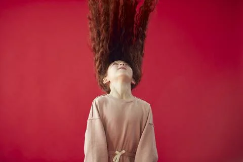 Young Girl With Long Red Hair Tossing It In The Air Against Red Studio Stock Photos