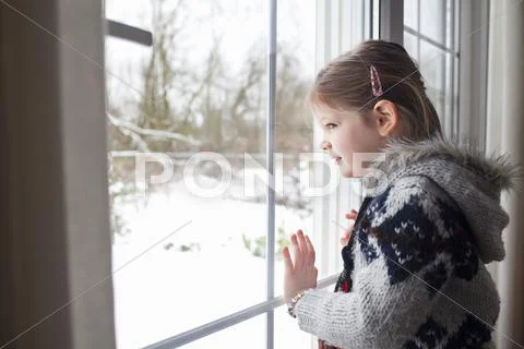 Young Girl Looking Out Of Window At Garden In Snow
