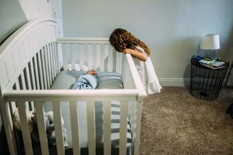 Young girl looking over the crib at newborn sibling Stock Photos