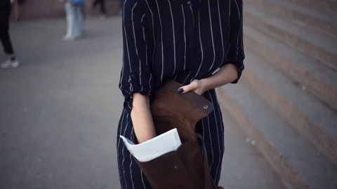 Young girl looking for something in her bag standing in a city park Video stock 79357487