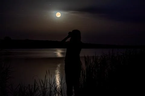 A young girl looks through binoculars at a beautiful huge moon in the night s Stock Photos