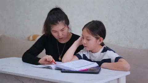Young girl loses focus while doing homework with tablet and book as mother tries Stock Footage 333483655