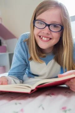 Young Girl Lying On Bed Reading Book Stock Photos