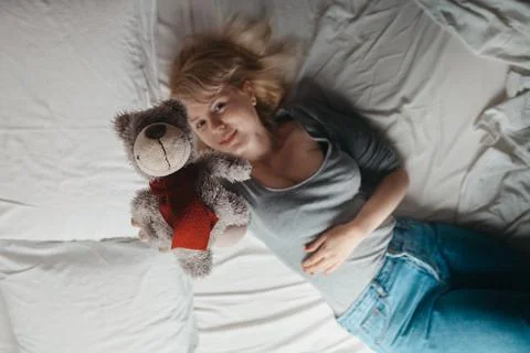 Young girl lying on bed with stuffed bear Stock Photos