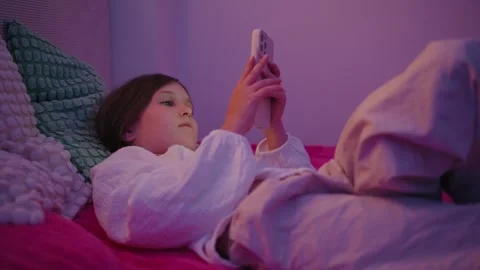 Young Girl Lying on Bed Using Smartphone in Bedroom with Neon Lighting Stock Footage 345528355