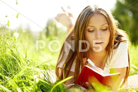 A young girl lying on grass and writing in a notebook Stock Photos