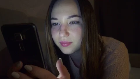A young girl is lying on the sofa, looking at the phone screen at night. Vídeo Stock 108752059