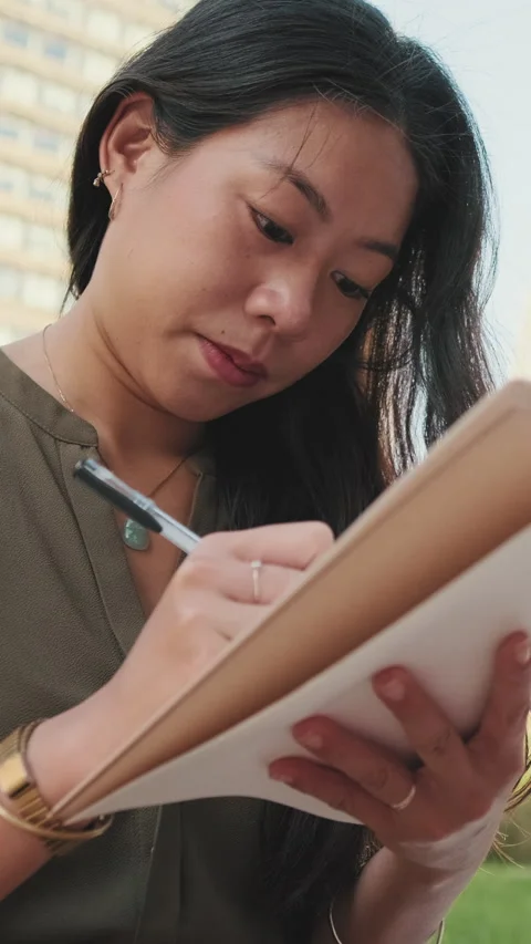 Young girl makes notes in notebook while sitting on modern buildings background Stock Footage 227024957