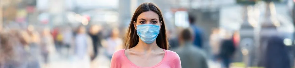 The young girl with medical mask on her face stands on the crowded street Stock Photos