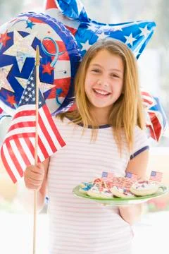 Young girl outdoors on fourth of July with flag and cookies smiling Stock Photos