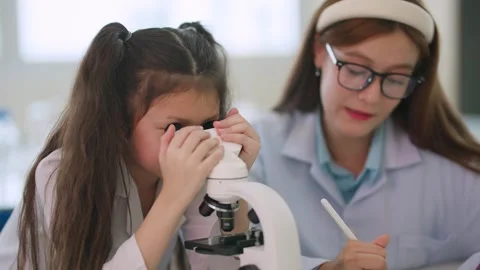 Young girl peers through microscope with curiosity Stock Footage 338011134