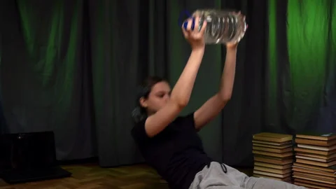 Young girl performs sit-ups with large bottle of water.Home Workout. Stock Footage 130966151