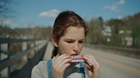 Young girl playing a red harmonica on a bridge 스톡 동영상 334100006