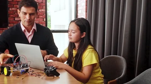 Young girl programs a robot with her teacher using a laptop in a modern class. 動画素材 313478400