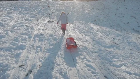 A young girl pulling a sledge up a wintery snowy hill. Winter Fun Stock Footage 147345765