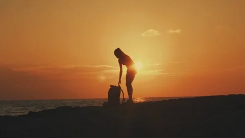 A young girl puts on her backpack at sunset or sunrise against the background of Stock Footage 78575324