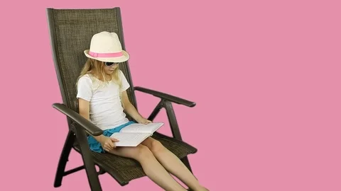 A young girl is reading a book sitting on a chair. Stock Footage