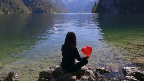 Young girl with red balloon in shape of heart in nature next to the lake. Stock Footage 75166331