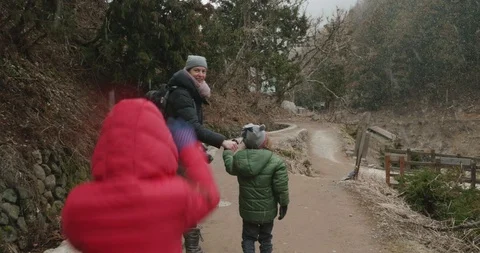 Young girl in red jacket hops and skips to catch up with her mother and brother Stock-Footage 108325552