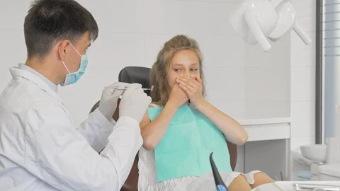 Young girl refusing showing teeth to a dentist covering her mouth with her hands Stock Footage 115044742