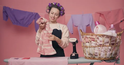 A young girl with rollers twisted on her head folds laundry irons blouses with a Stock Footage 218415917