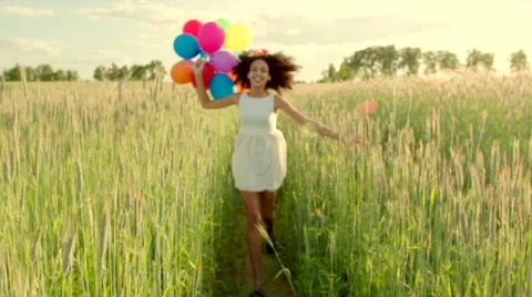 Young girl running through a wheat field with colour balloons during sunset Stock Footage 64773364