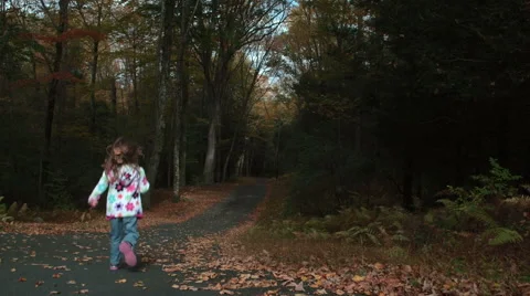 Young girl runs down a leaf-covered road Stock Footage 44114175