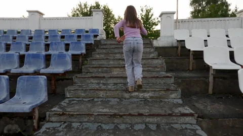 Young girl runs energetically up and down the bleachers in a sports stadium. Stock Footage 283671753