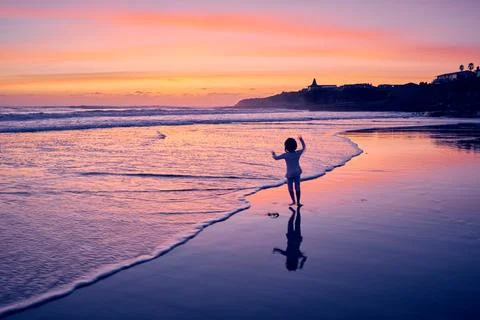 Young girl runs happily with arms up during dusk on a beach. Stock Photos