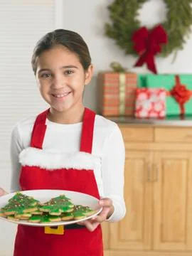 Young girl in a Santa apron holding a plate of Christmas cookies Stock Photos