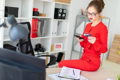 The young girl sat down on the table in her office and held a credit card ... Stock Photos