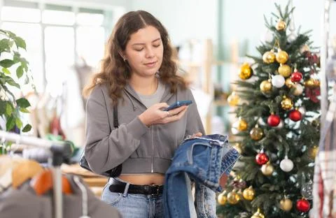 Young girl scanning QR-code on jeans pantaloons in clothing store during Stock-Fotos