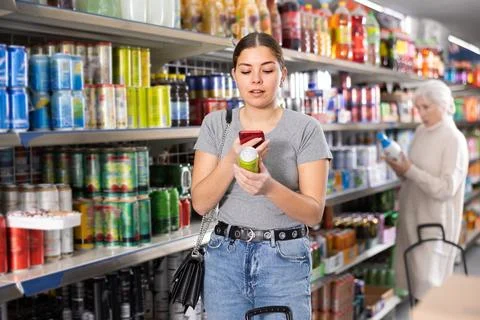Young girl scanning QR code with phone on tin can of soft drink Foto stock