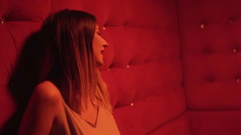 Young girl singing on a sofa in red room of nightclub. Shooting music video Stock Footage 221016432