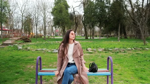 Young girl sits on bench park. Brunette woman walks towards bench and sits down Stock Footage 152111953