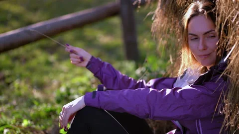 Young girl sits under a haystack with a straw. There's a fence in the background Stock Footage 139455328