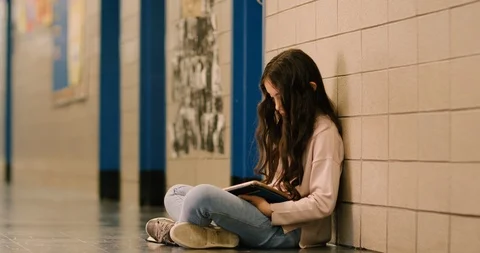 Young girl sitting and using a tablet in a school hallway Stock Footage 108793772