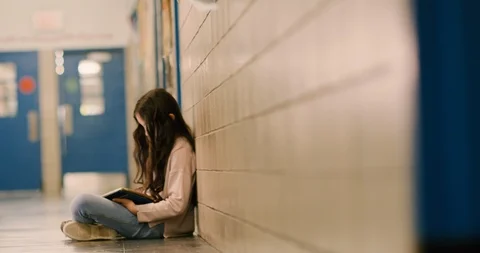 Young girl sitting and using a tablet in a school hallway Stock Footage 108793994