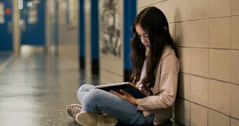 Young girl sitting and using a tablet in a school hallway Stock Footage 108795451