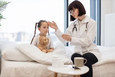 Young girl sitting in bed while nurse checking temperature Stock Photos