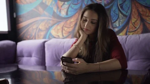 A young girl is sitting at a cafe table, with a smartphone in her hands Stock Footage 74308742