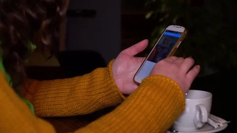 Young girl sitting in cafe at table and uses a smartphone. The girl is revising Stock Footage 82007485
