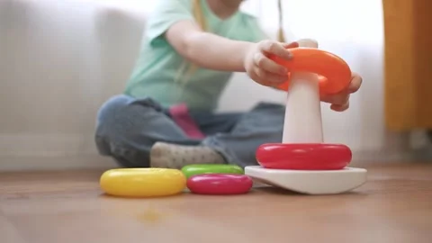 Young girl sitting on the floor with stack of colorful toys. Child plays the Video stock 317714740